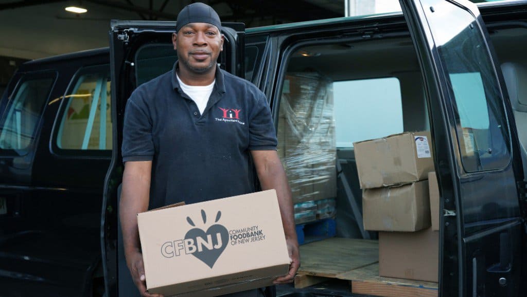 Man stands in front of van holding a CFBNJ box full of food.