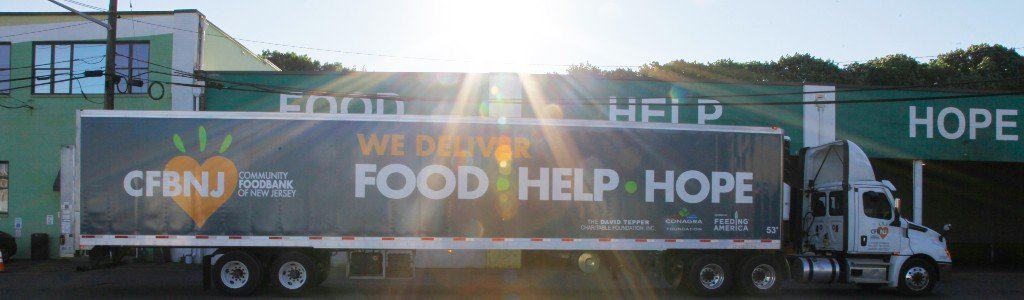 Truck parked in front of warehouse with the sun in the background. The truck says "we deliver food, help and hope"