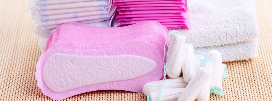 Pink maxi pads, liners, and tampons stacked up with washcloths and towels