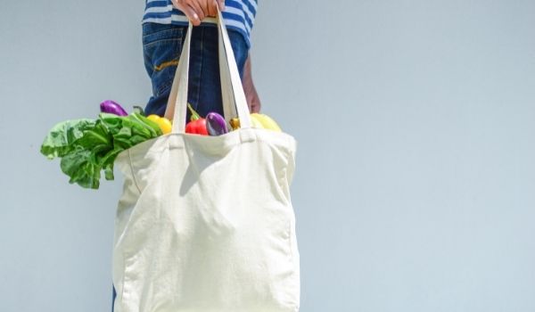 Person carrying a cloth shopping bag full of fruit and vegetables