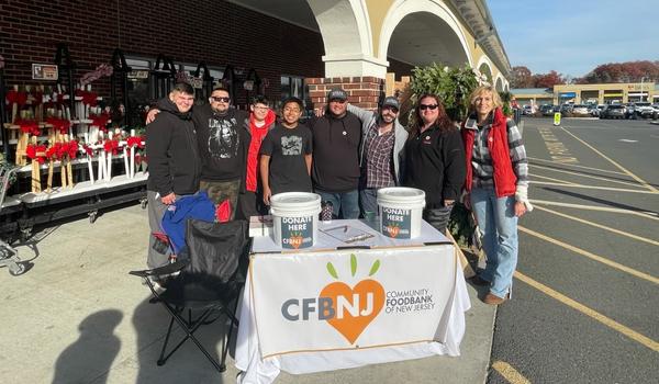 People in front of a grocery store at a table with donation buckets. The table is labeled CFBNJ.